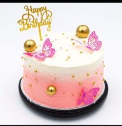 Round Egg Free pink ombre celebration cake decorated with butterfly toppers, edible gold pearls, gold spheres and a Happy Birthday topper.