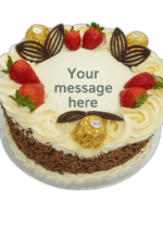 Round white celebration cake topped with fresh strawberries, Ferrero Rocher chocolates, dark chocolate leaf decorations, whipped cream swirls, chocolate flakes around the sides, and a blank center for a personalized message.
