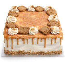 Square fresh cream caramel cake with a rich caramel drip, caramel glaze, fresh cream swirls, and biscuit pieces on top.