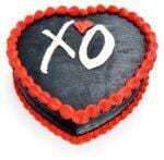 Top view of a heart-shaped black fresh cream cake with red borders and a personalised XO design.