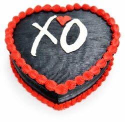 Top view of a heart-shaped black fresh cream cake with red borders and a personalised XO design.