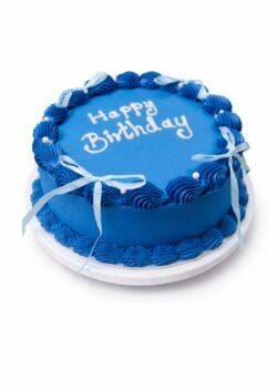 Top view of a royal blue fresh cream birthday cake featuring shell borders, white ribbon bows, pearl accents, and custom birthday writing.