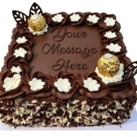 Square chocolate celebration cake with smooth chocolate frosting, Ferrero Rocher chocolates, chocolate leaf decorations, white cream flowers, mixed chocolate curls around the sides, and a personalised message area in the centre.