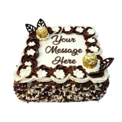 Square fresh cream celebration cake decorated with chocolate and vanilla swirls, white floral piping, Ferrero Rocher chocolates, chocolate leaf decorations, milk and white chocolate shavings, and a personalised message.