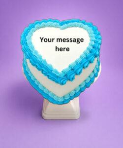 Blue heart-shaped birthday cake with smooth white icing, vibrant blue piped borders, and space for a personalised celebration message.