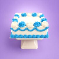 Blue and white square celebration cake with smooth vanilla cream frosting, alternating blue and white buttercream rosettes, blue wave piping around the sides, blue shell border at the base, and a large blank centre ready for a personalised edible photo or custom message.