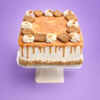 Square fresh cream caramel cake with a rich caramel drip, caramel glaze, fresh cream swirls, and biscuit pieces on top.