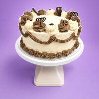 Classic Chocolate & Vanilla Celebration Cake decorated with smooth vanilla buttercream, chocolate buttercream swirls, elegant chocolate piping, chocolate decorations, and a plain centre for a personalised message. Freshly made in Sheffield.