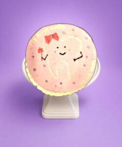 Round pink tooth-themed birthday cake with adorable tooth character and personalized message