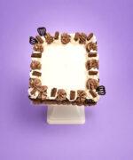 Square egg-free chocolate celebration cake decorated with fresh dairy topping, chocolate piping, premium chocolate curls covering the sides, chocolate curl pieces, decorative chocolate fans, and a large space for a personalised edible birthday message.