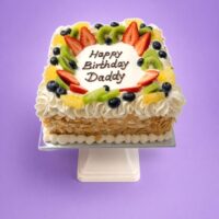 Egg-free fresh fruit celebration cake topped with strawberries, kiwi, blueberries, orange segments, cream piping and almond flakes with a personalised birthday message.
