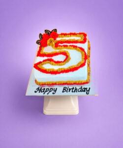 Egg-free number 5 birthday cake decorated with red and gold cream piping, floral decorations and chocolate accents.