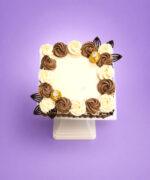 Top view of a square Ferrero chocolate celebration cake decorated with alternating chocolate and vanilla whipped frosting rosettes, Ferrero Rocher chocolates, elegant chocolate leaf decorations, and a smooth centre for a personalised birthday or celebration message.