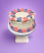 Round fresh cream cake decorated with pink and lavender fresh cream rosettes, white floral accents, textured white sides, and space for a personalised message.