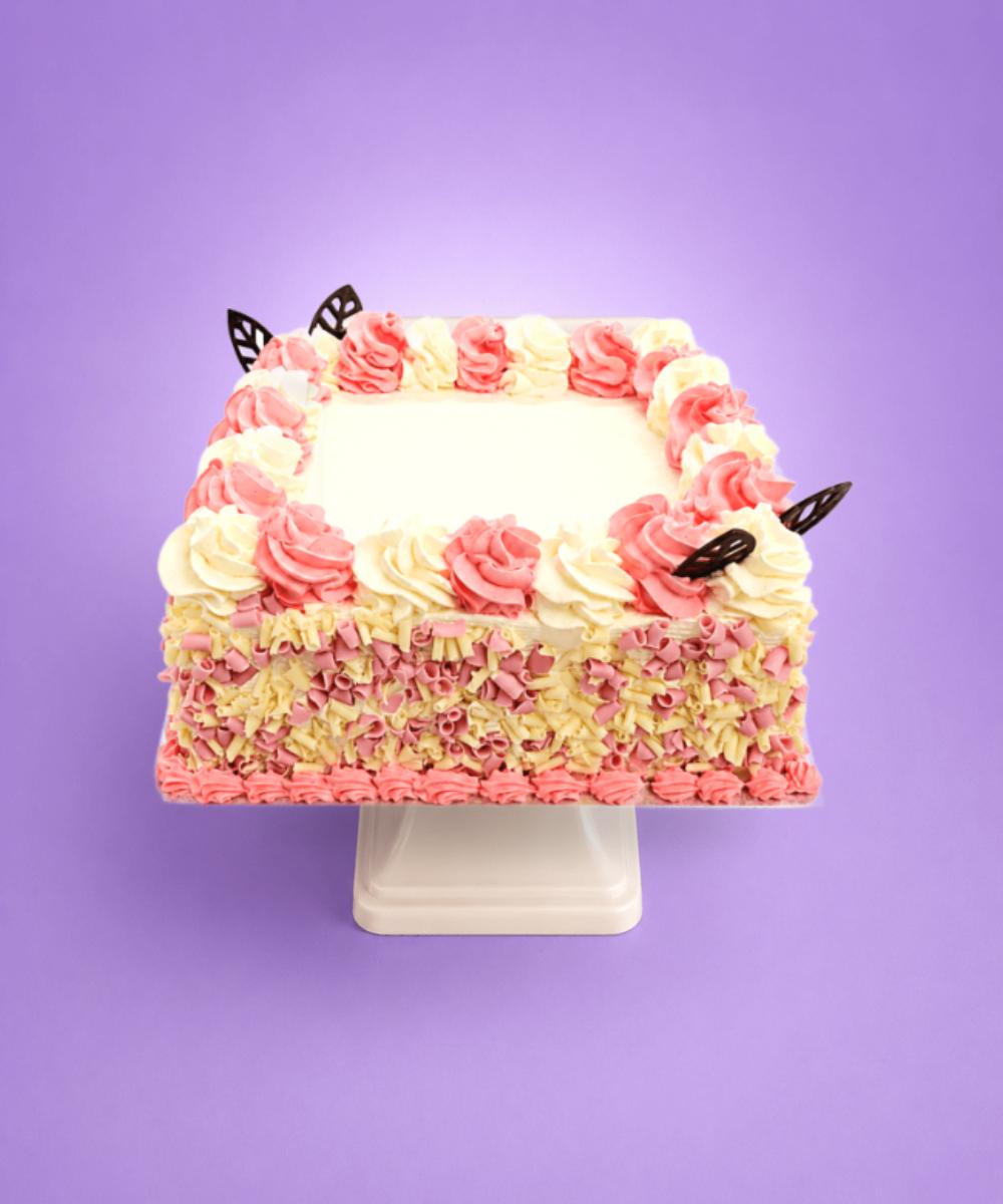 Pink & White Chocolate Curl Celebration Cake. Pink and white celebration cake decorated with whipped frosting swirls, pink and white chocolate curls around the sides, chocolate leaf decorations, and a smooth personalised message area for birthdays and special occasions.