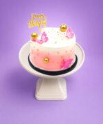 Round Egg Free pink ombre celebration cake decorated with butterfly toppers, edible gold pearls, gold spheres and a Happy Birthday topper.