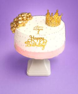 Pink and gold princess crown birthday cake decorated with a luxury gold crown topper, gold spheres, edible pearl details and personalised birthday message.