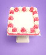 Top view of a square pink and white celebration cake featuring alternating pink and white buttercream swirls surrounding a smooth blank centre designed for a personalised edible image or celebration message.