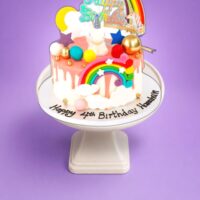 Personalised Rainbow Unicorn Birthday Cake decorated with rainbow, unicorn figurine, colourful drip finish, clouds, stars and birthday message.