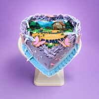 Heart-shaped Stardew Valley celebration cake with pastel lavender fresh cream, edible game image, butterflies, ribbon bows and pearl decorations by Cake Palace.