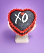 Heart-shaped fresh cream cake with a black finish, red piped border, and personalised XO message.