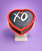 Top view of a heart-shaped black fresh cream cake with red borders and a personalised XO design.