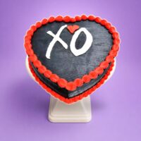 Top view of a heart-shaped black fresh cream cake with red borders and a personalised XO design.